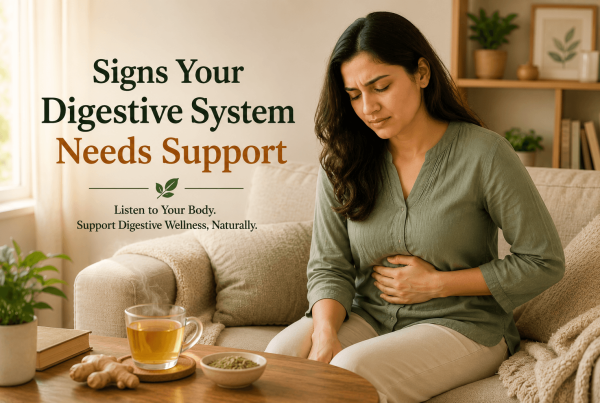 Person sitting on a couch with a hand on their stomach and a cup of ginger tea nearby, illustrating early signs that the digestive system may need support in a calm home setting.